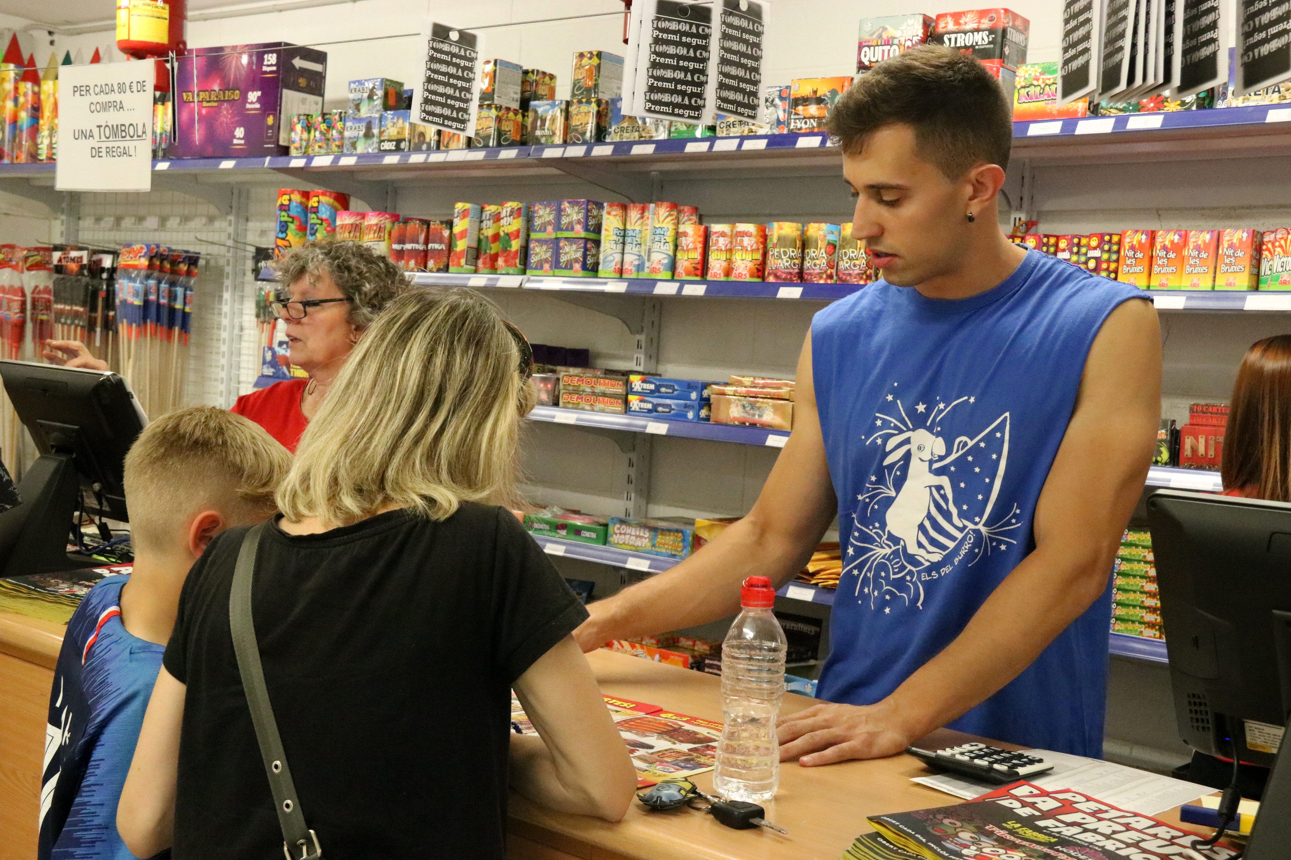 Un vendedor de una tienda de petardos atendiendo una familia durante la campaña de la verbena de San Juan | ACN