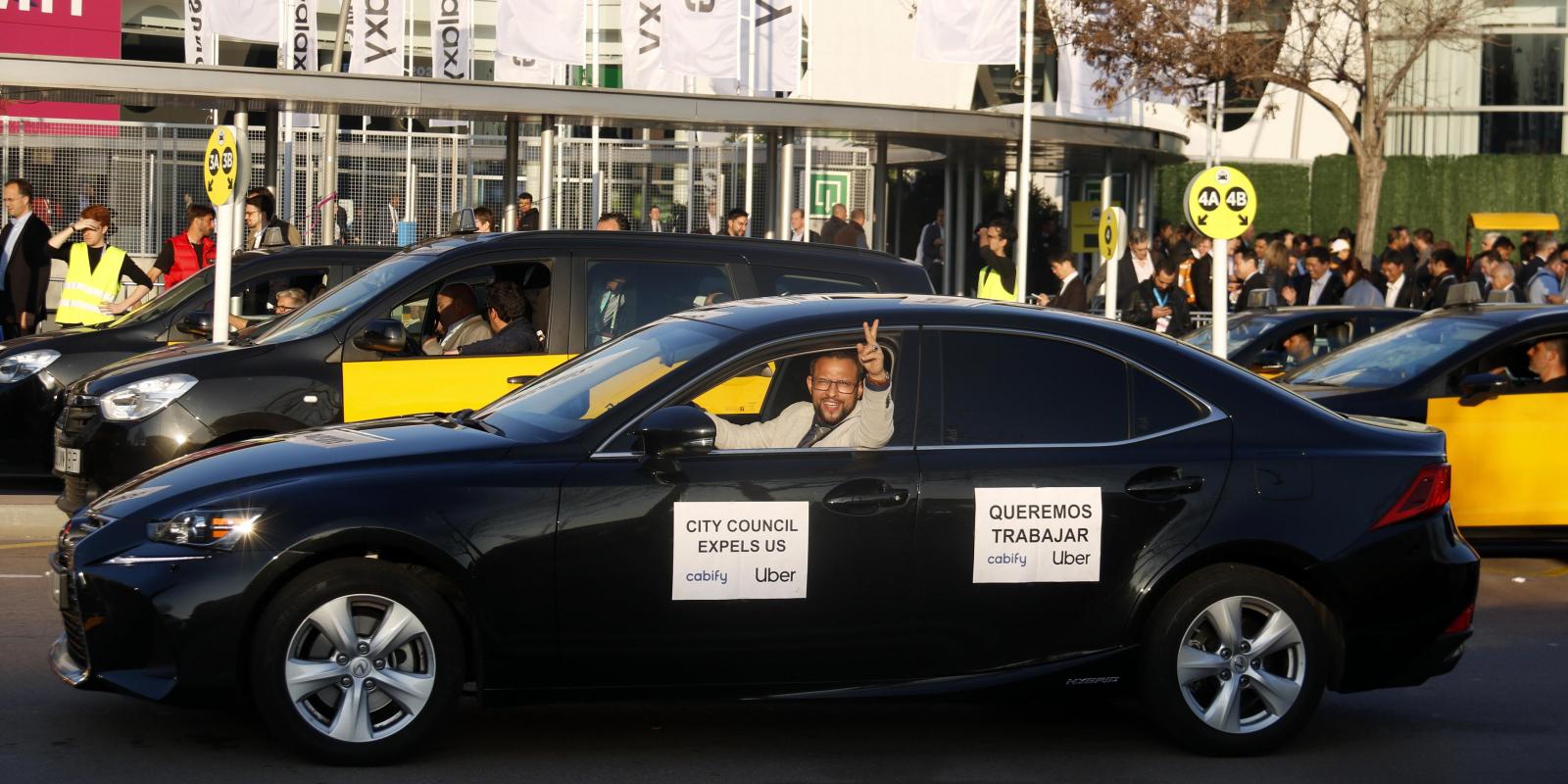 Un VTC amb un cartell on hi posa "volem treballar", amb taxis de fons | ACN