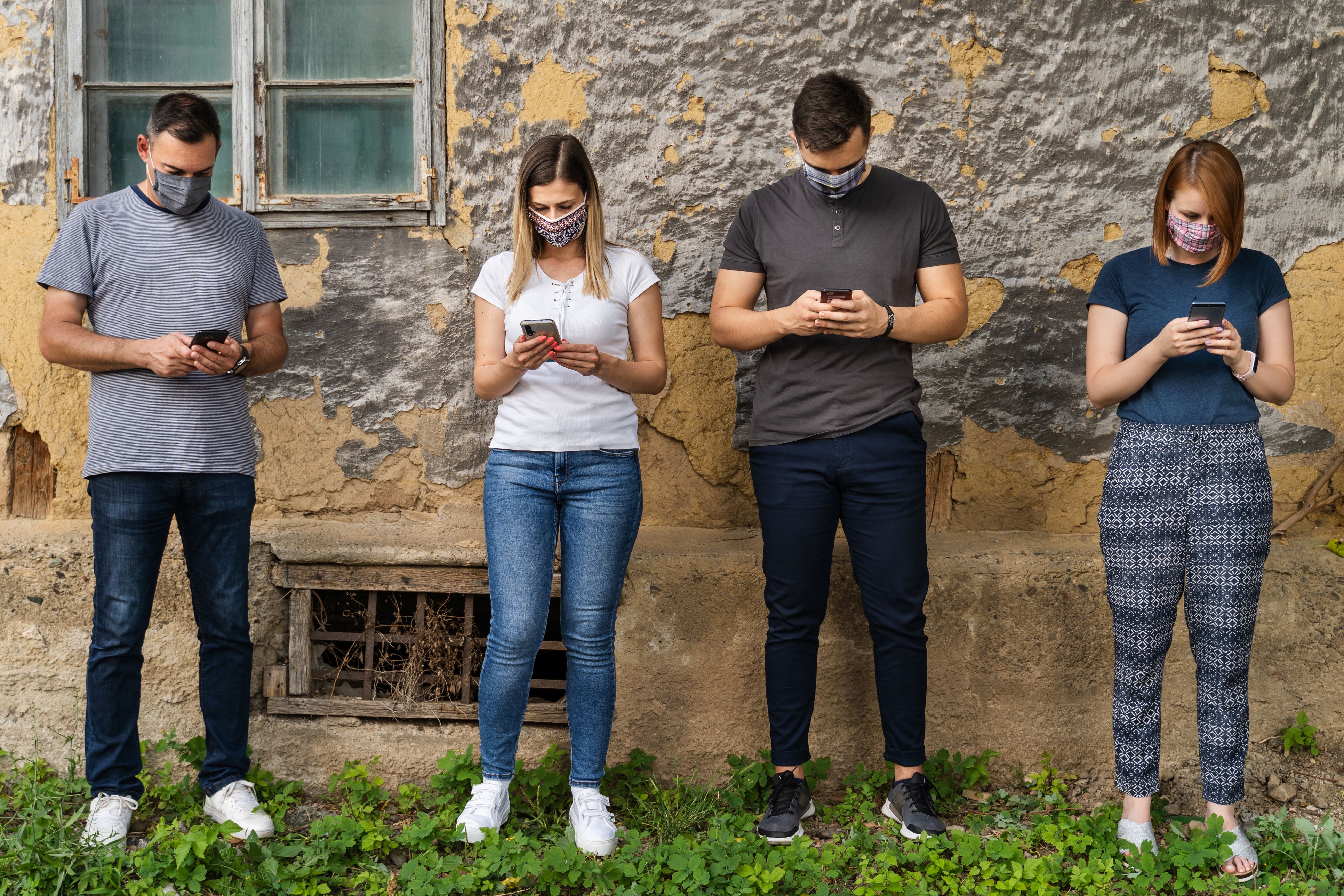 Jóvenes con distancia y mascareta mirando su smartphone | iStock