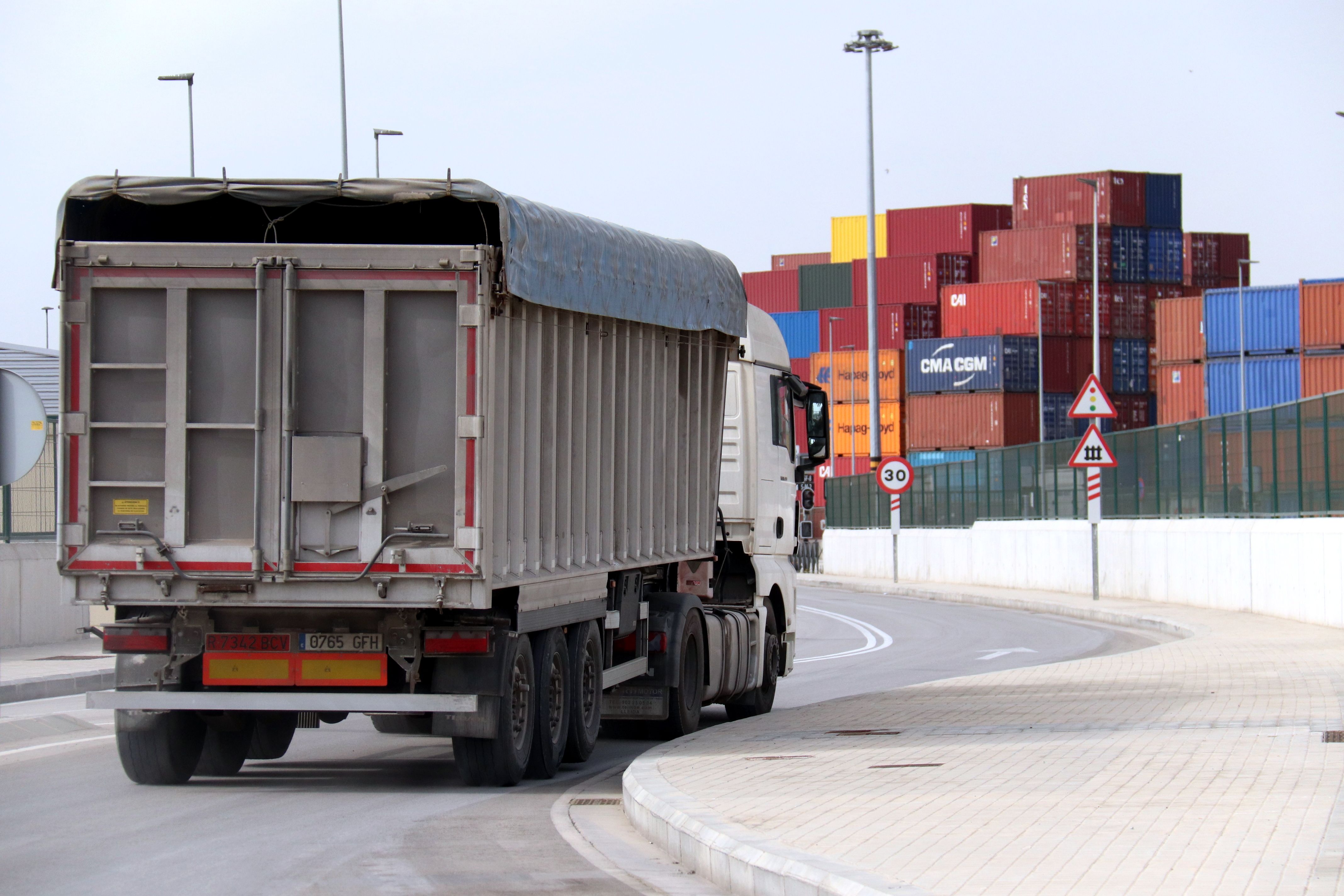 Un camió surt del port de Barcelona, amb contenidors per a exportacions al fons | ACN