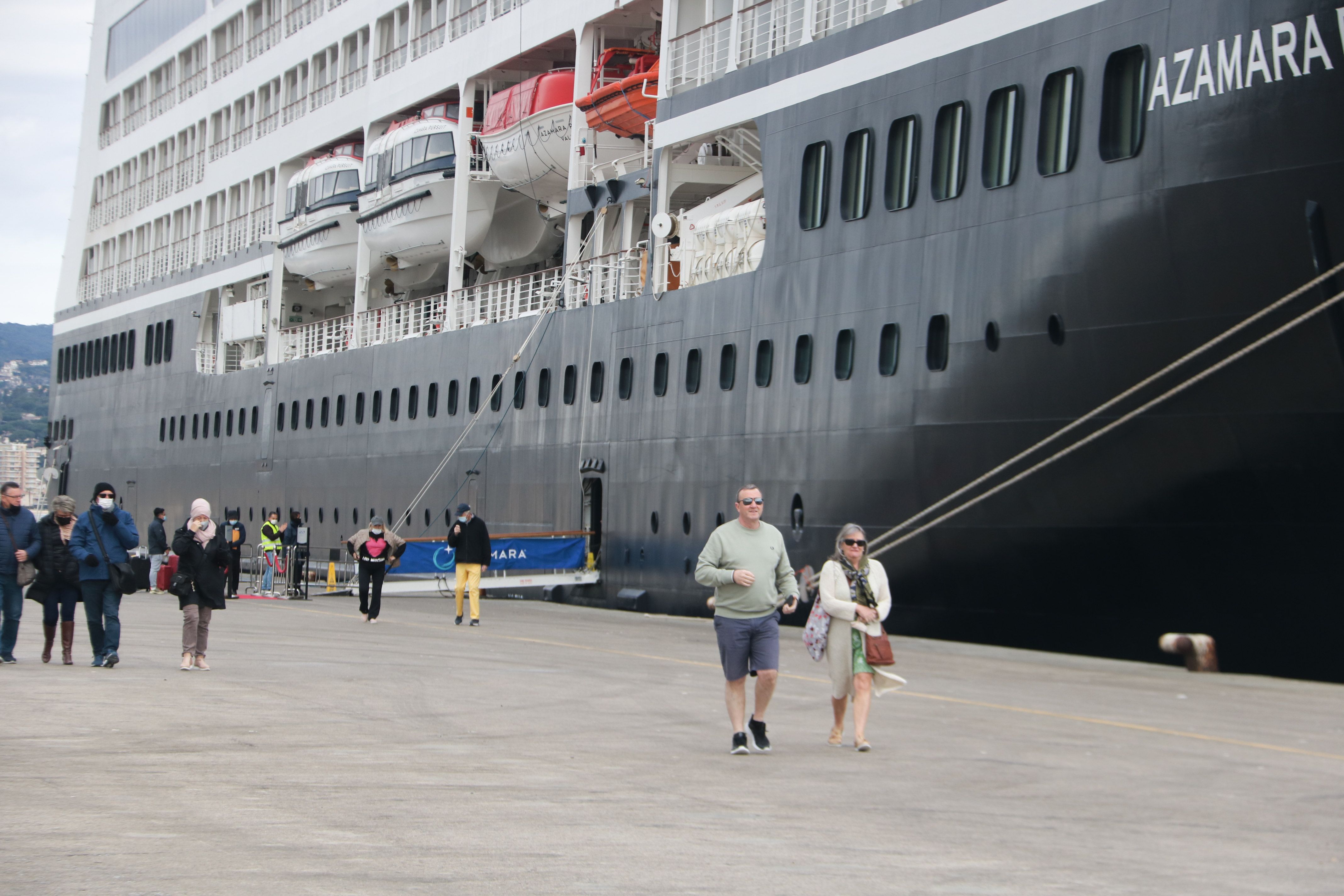 Dos passatgers baixen de l'Azamara Pursuit i caminen cap al Port de Palamós | ACN