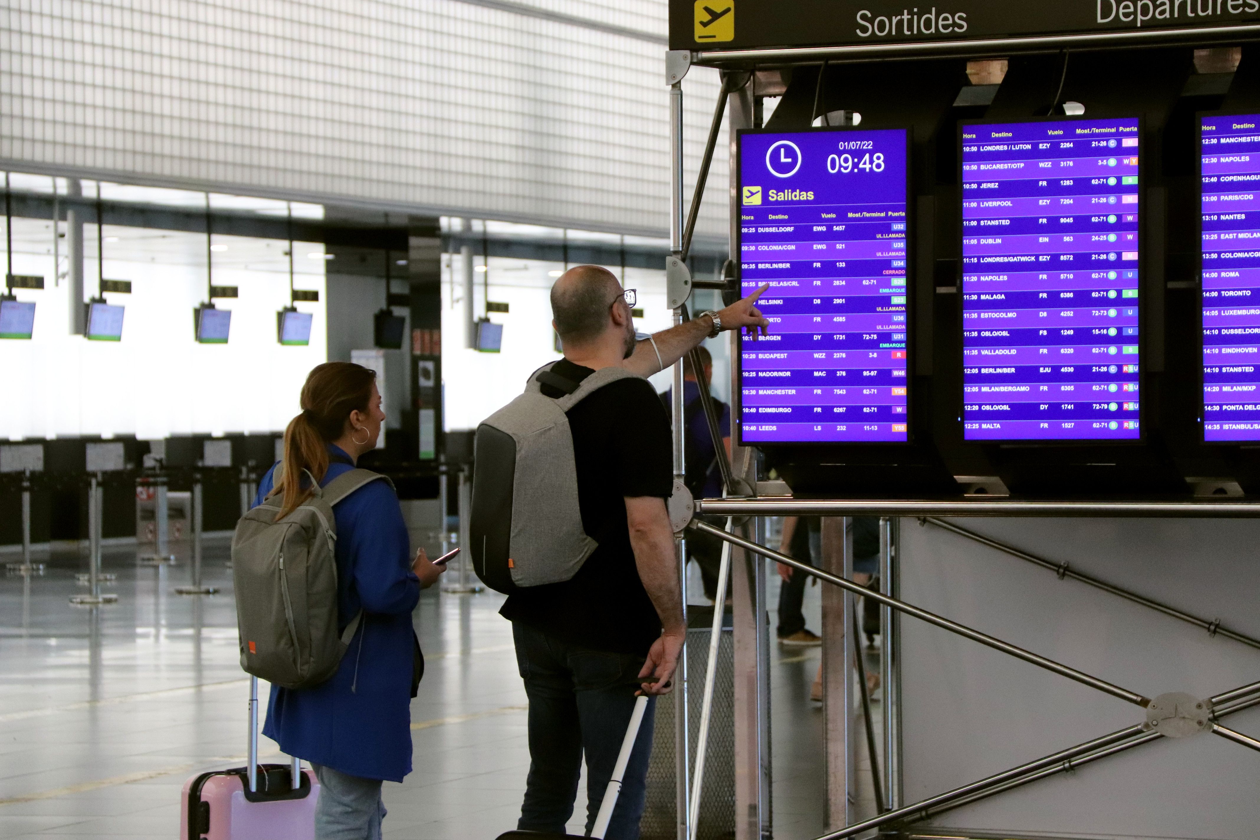 Dos turistas mirando el mostrador de información de vuelos en el aeropuerto de El Prat | ACN