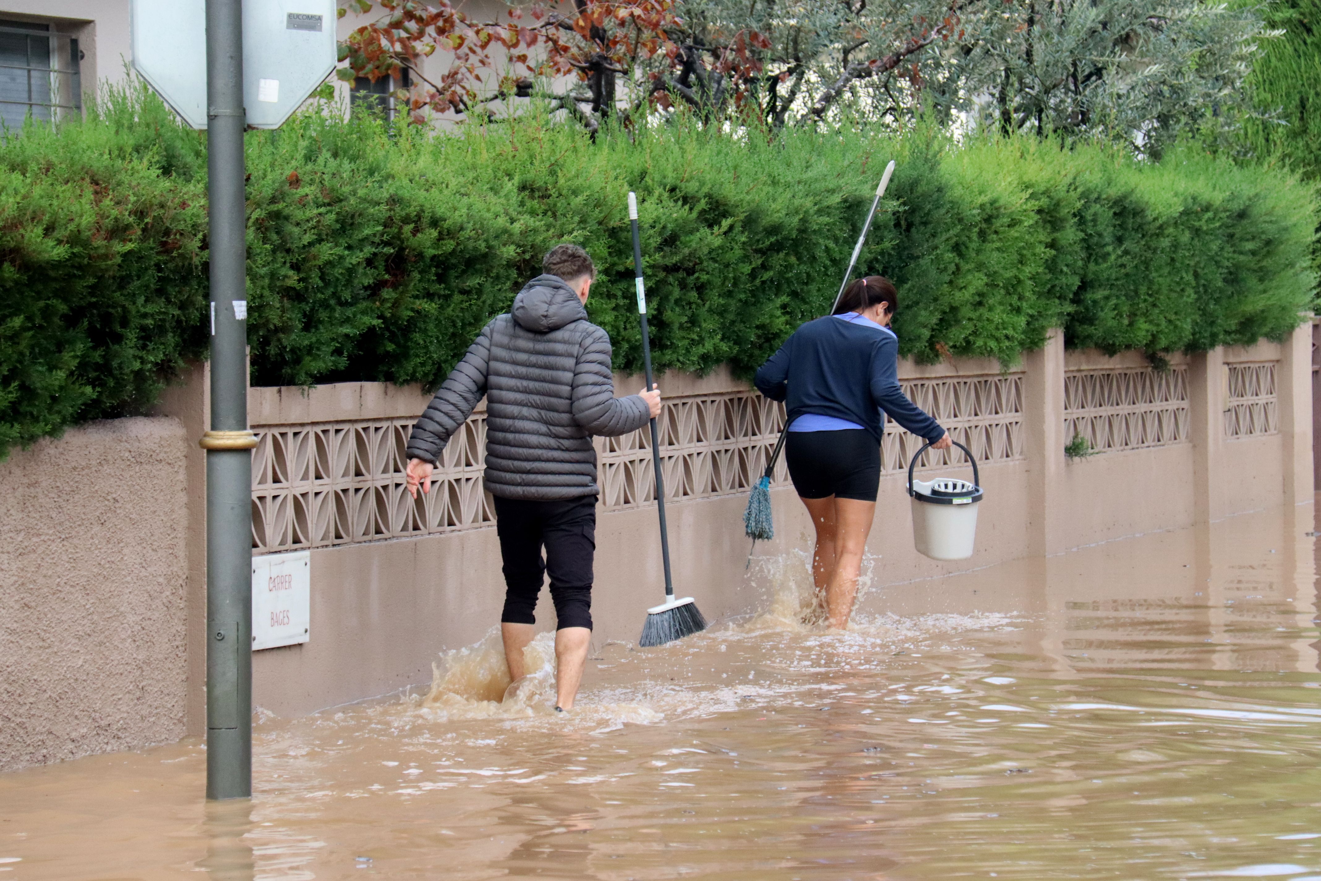 Dos veïns caminant amb cubells per un dels carrers inundats de la urbanització La Móra de Tarragona | ACN