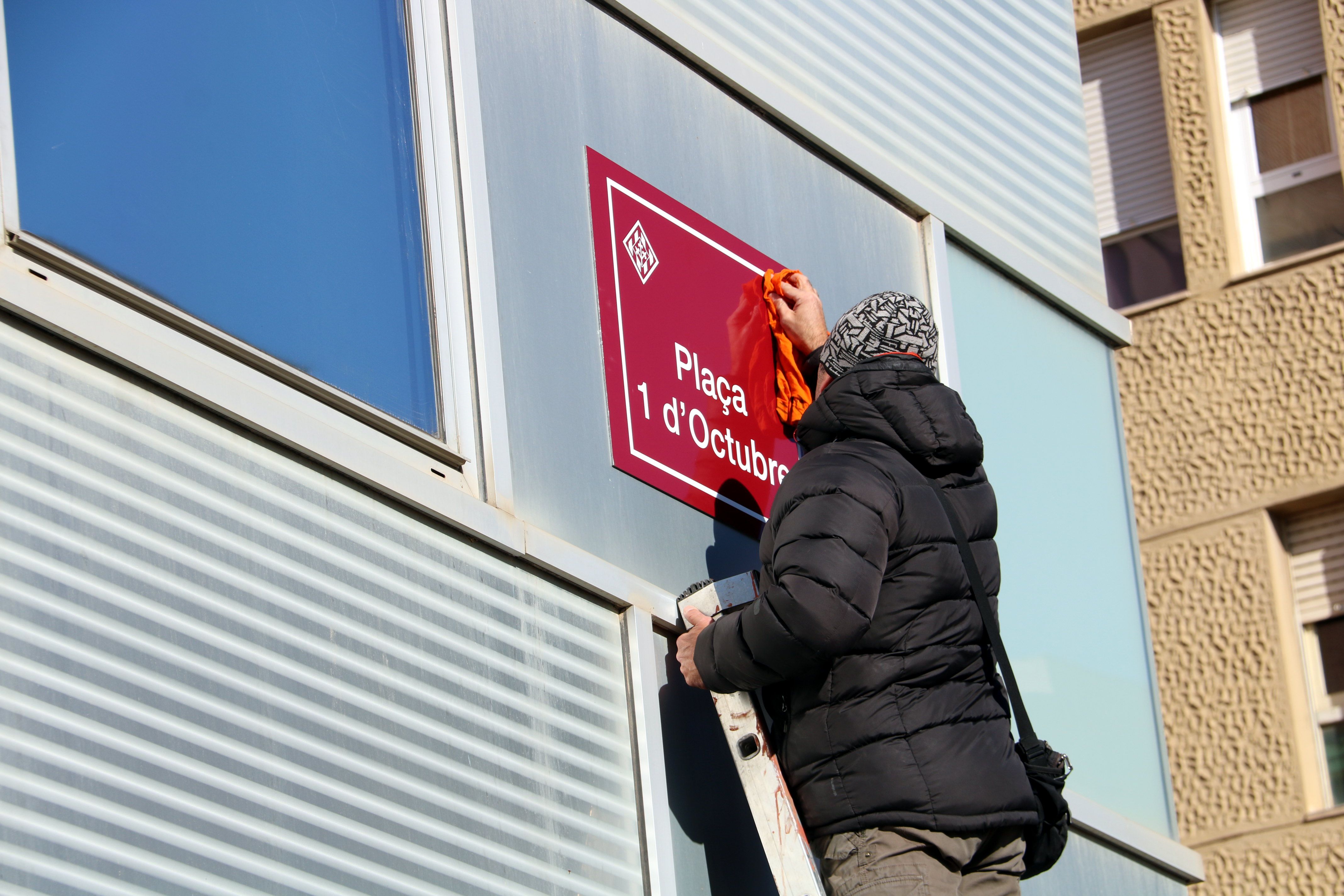 Un veí enfilat a l'escala que neteja el nou cartell de la plaça 1 d'octubre a Cappont | ACN