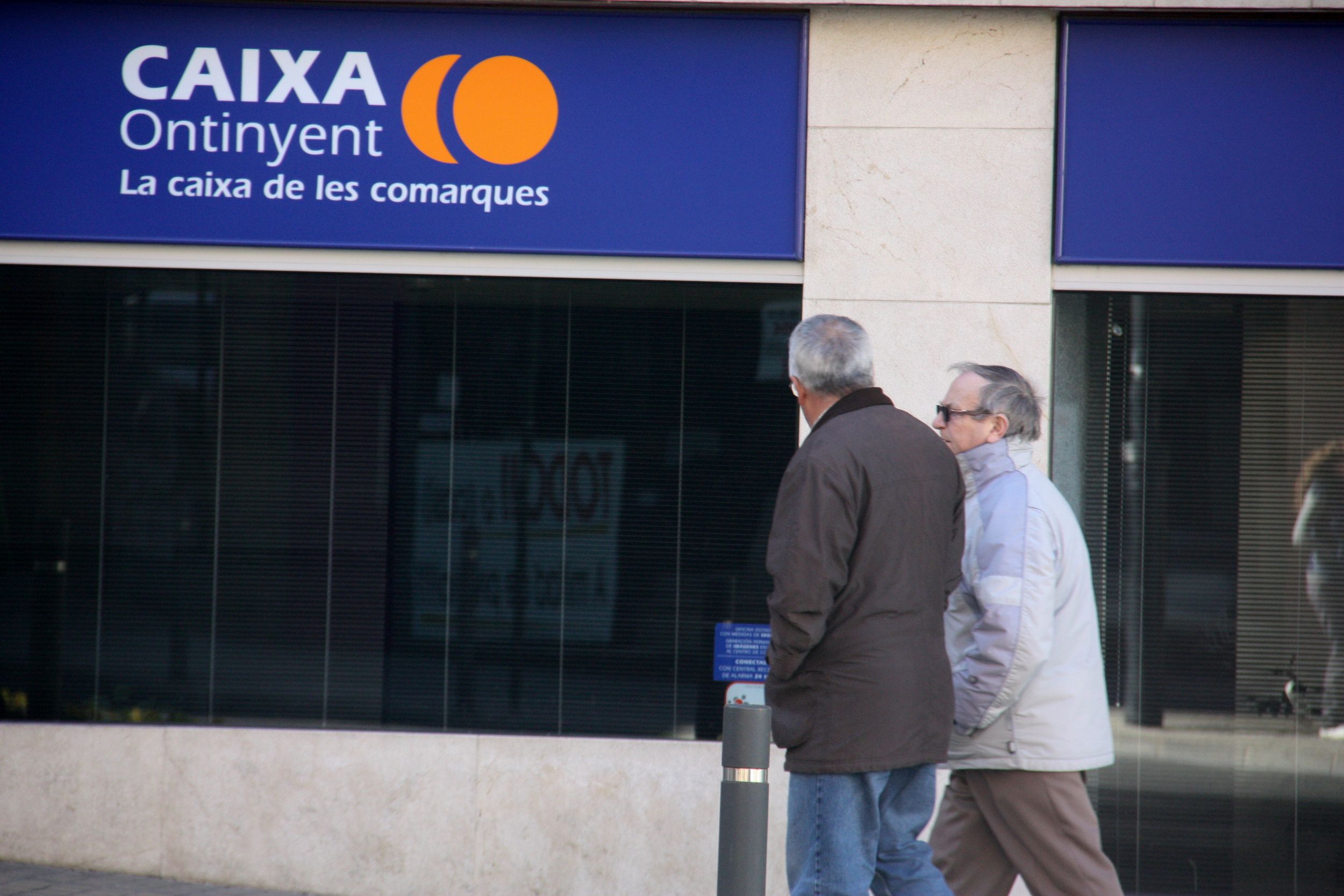 Dos persones passen per davant d'una oficina de Caixa Ontinyent a Ontinyent | ACN